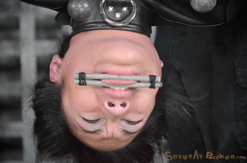 Dark-haired Asian hangs upside down in leather straitjacket